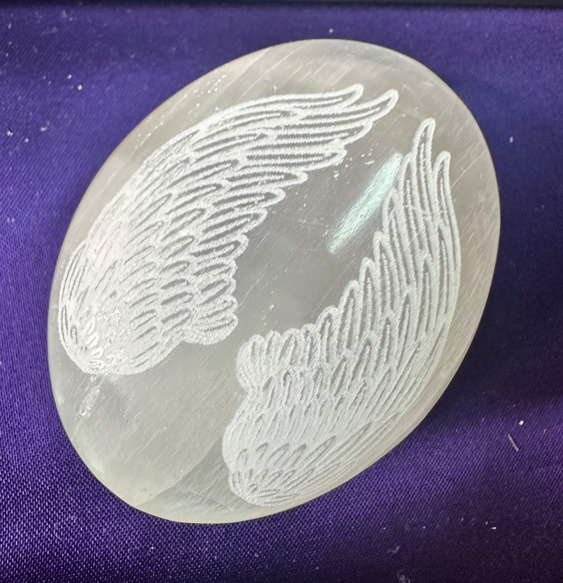 Selenite Palm Stone engraved with wings on a purple satin background